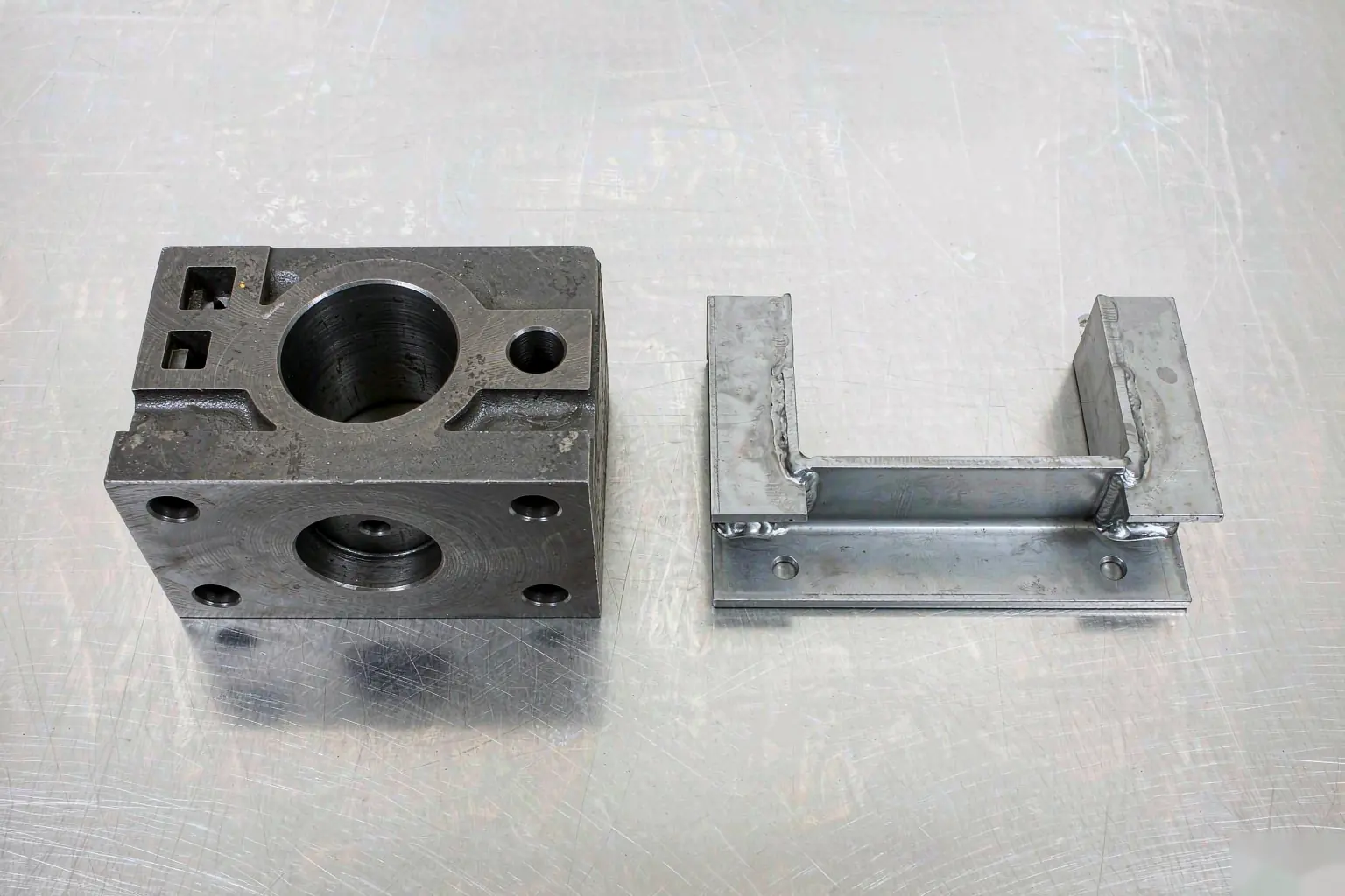 casting vs fabrication cost comparison: machined cast housing and welded bracket assembly on an inspection bench