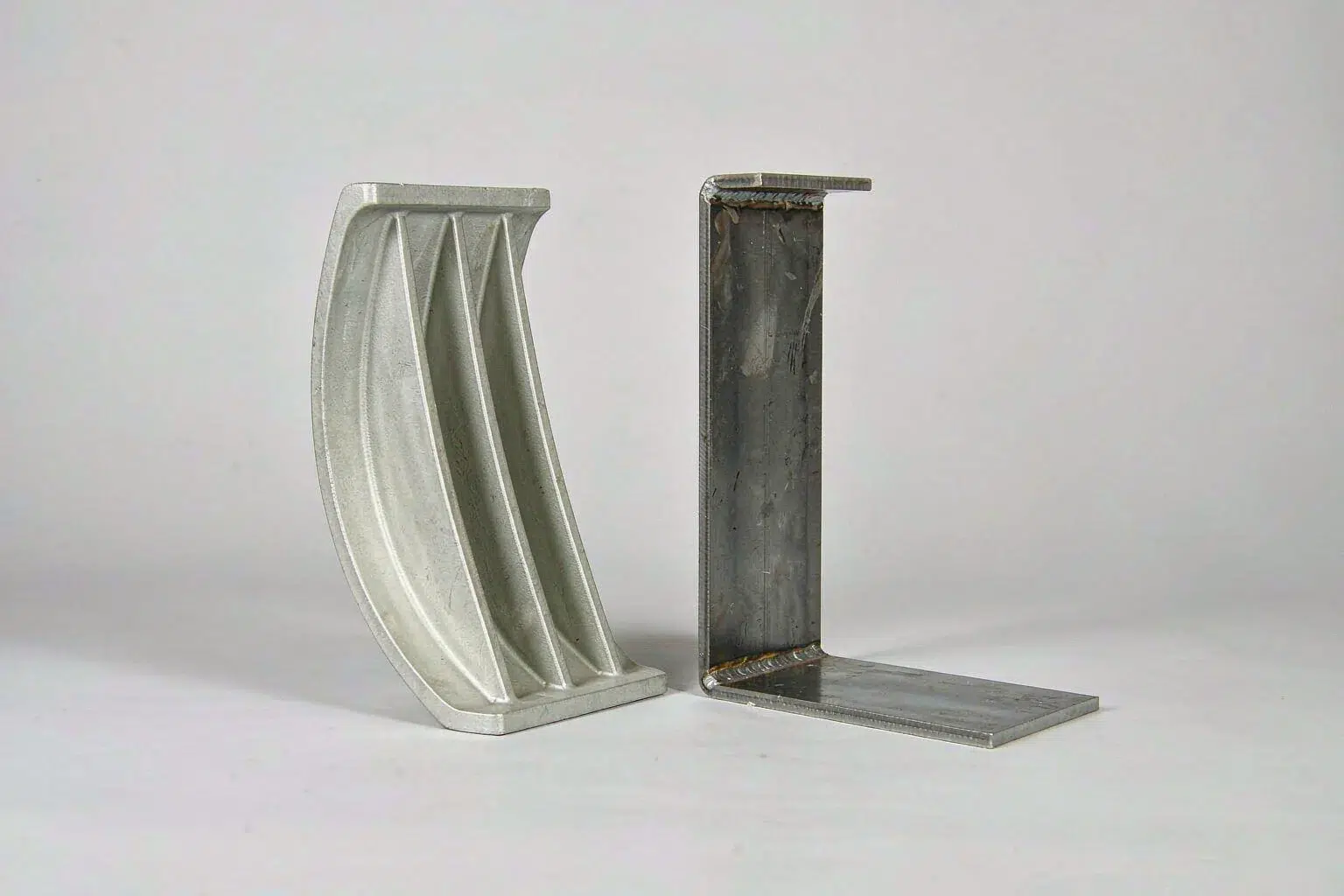 casting vs fabrication decision: cast aluminum bracket with cast ribs beside a welded steel bracket made from cut plates