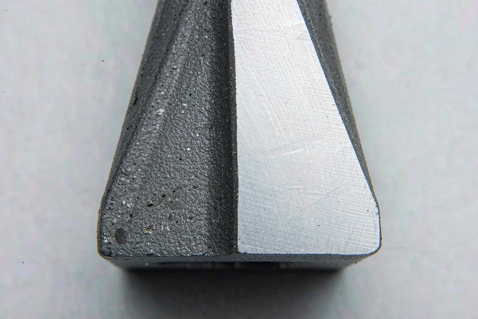 casting machining allowance close-up: machined bright metal face beside rough as-cast sand surface on an iron casting